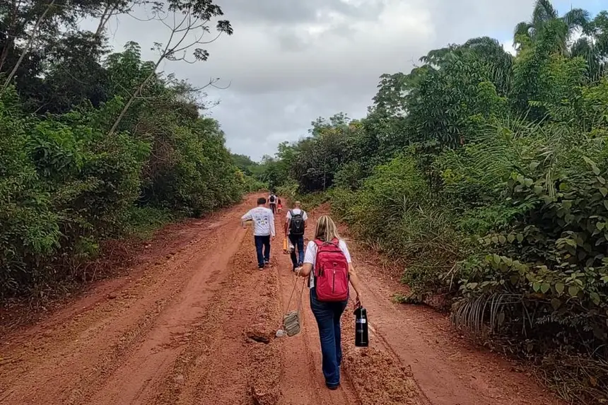 Estrada de terra em meio a mata com pessoas seguindo por ela em tempo nublado